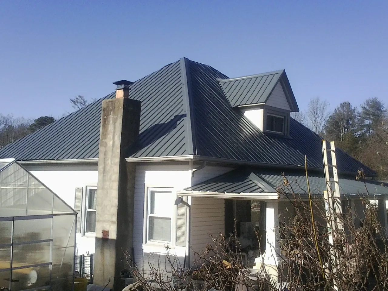 Dark blue standing seam metal roof on a white farmhouse with dormer — Slate & Tile Roof Repair by Roofing Brothers in Hoskins