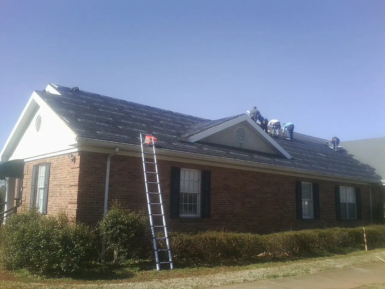 Crew tearing shingles off a brick ranch roof with a ladder set — Metal Roof Repair work by our crew in Hoskins