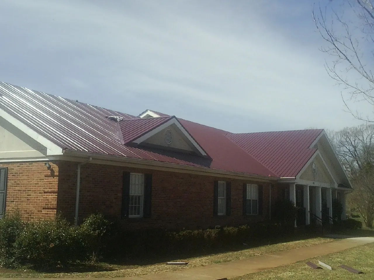 Red metal roof with gabled entries on a long brick building, from a Hail Damage Roof Repair job in Hoskins