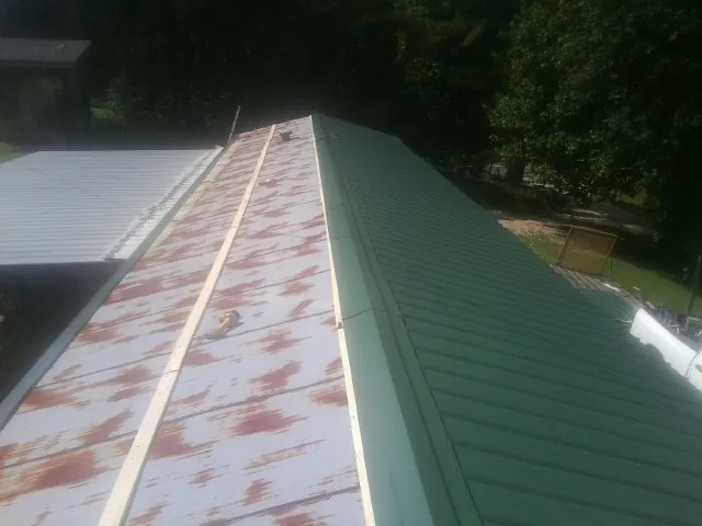 Old rusted panels beside newly installed green metal roofing — Wind Damage Roof Repair by Roofing Brothers in Hoskins