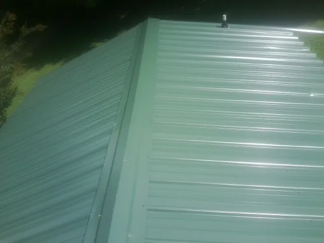 New green metal panels meeting at the ridge of a roof — Flat Roof Repair work by our crew in Hoskins