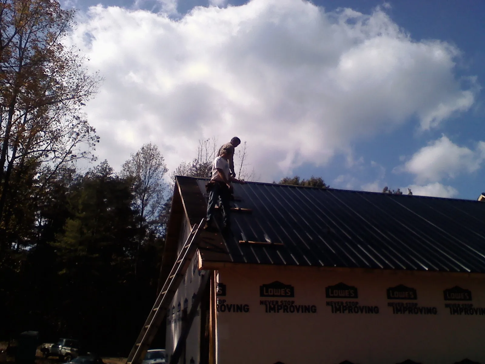 Roofer fastening dark metal panels high against a cloudy sky, from a Roof Inspection job in Hoskins