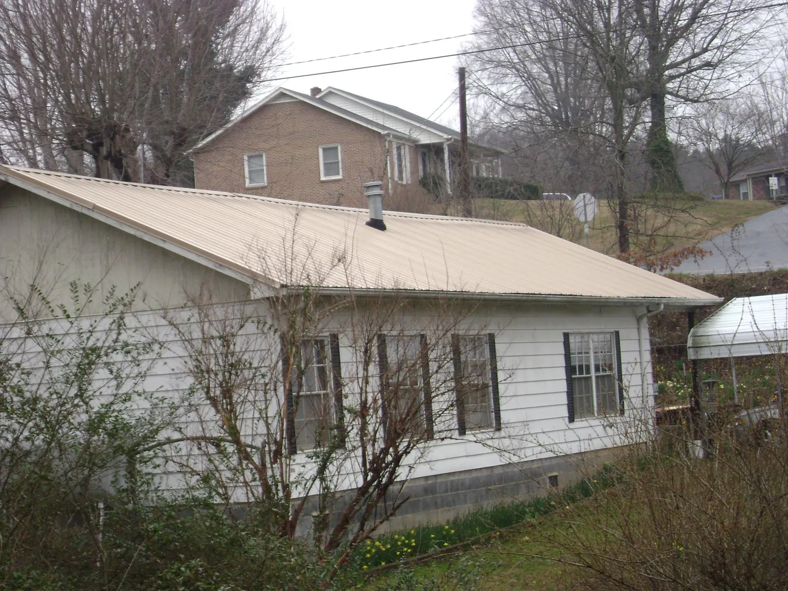 Tan metal roof on a white sided house set into a hillside — Commercial Roofing by Roofing Brothers in Hoskins