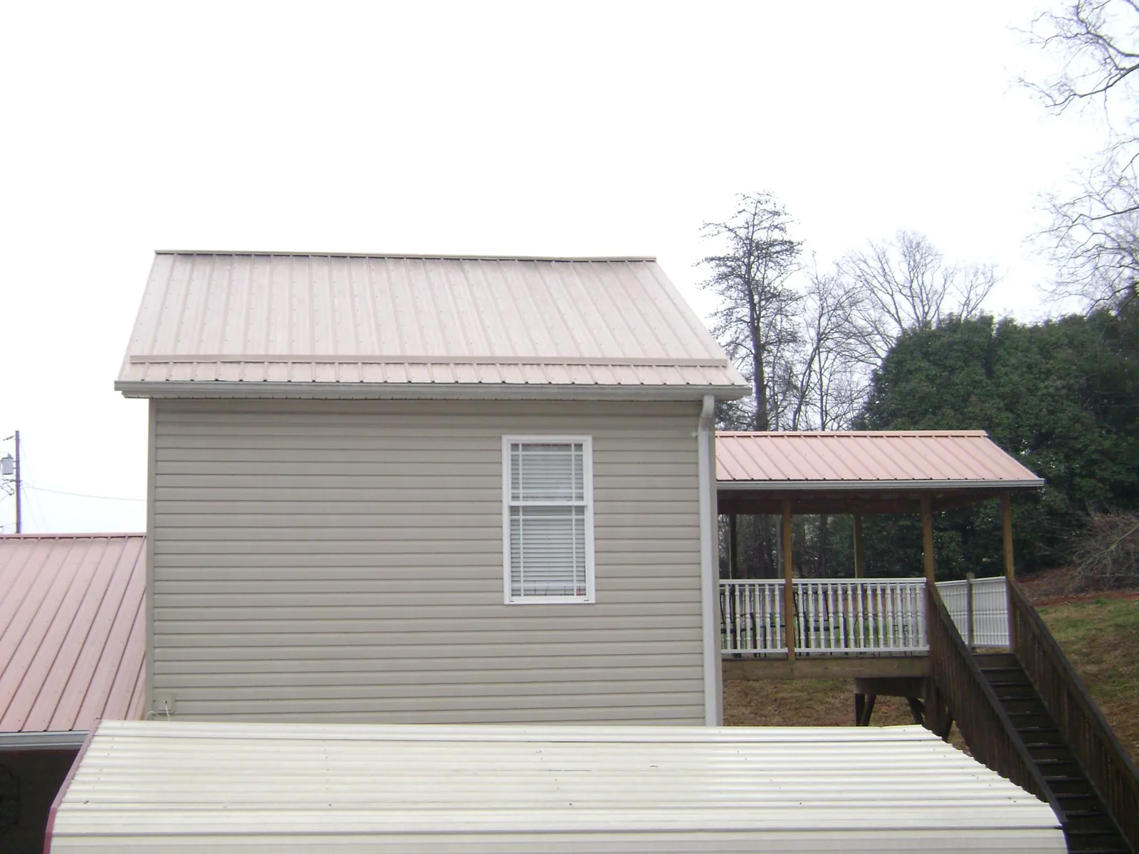 Tan metal roofs on a two story addition and attached porch, from a Roof Replacement job in Hoskins