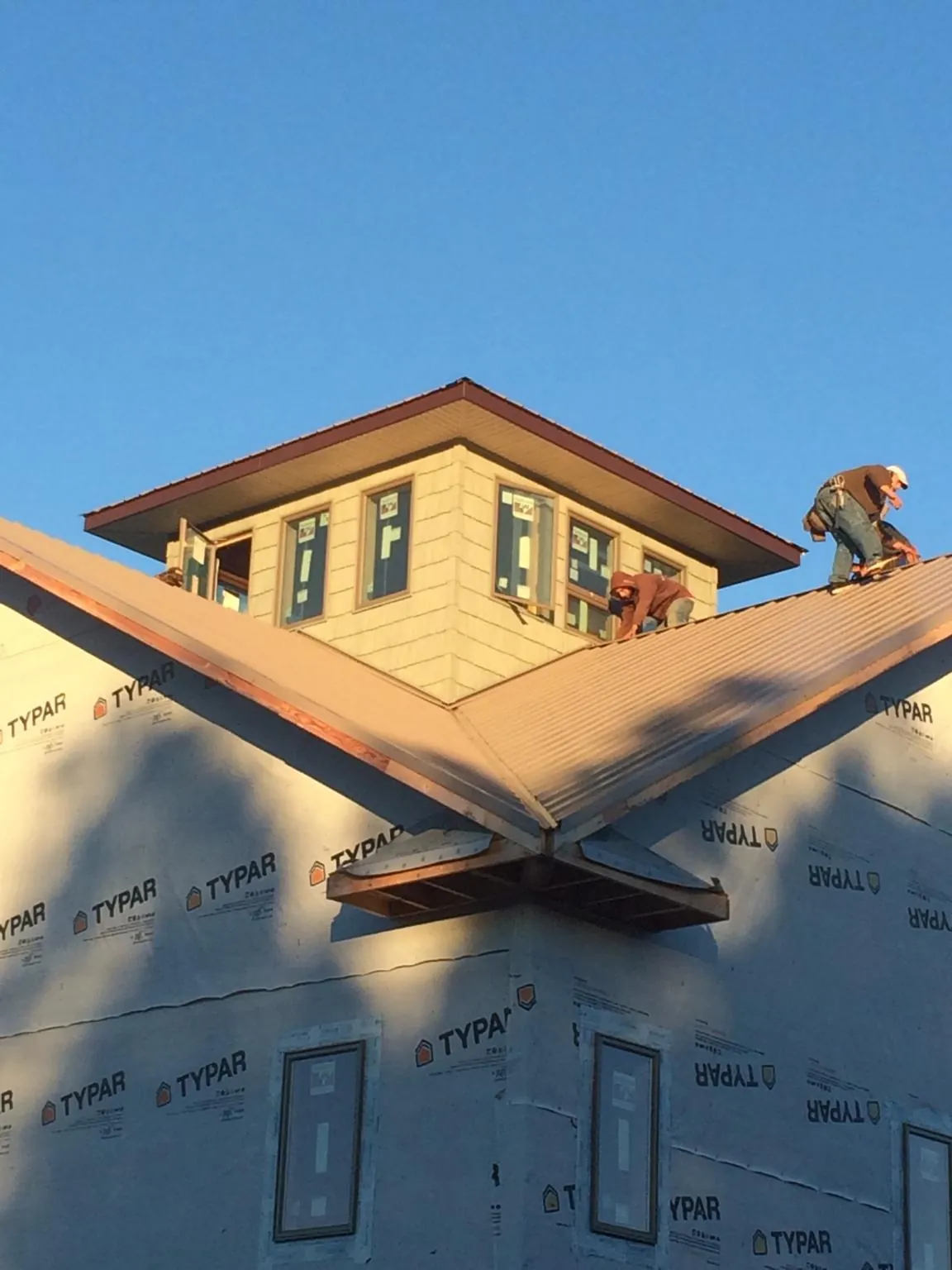 Roofers working around a rooftop cupola on a new metal roof at sunset — Roof Waterproofing in Hoskins by Roofing Brothers